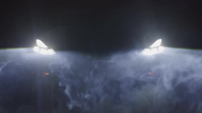 A medium abstract view shows the very bright white headlights of a car shining through plumes of white smoke or fog in a dark environment