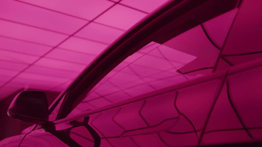 The frameless window of a modern car rolls down as a vivid pink light reflects off the body