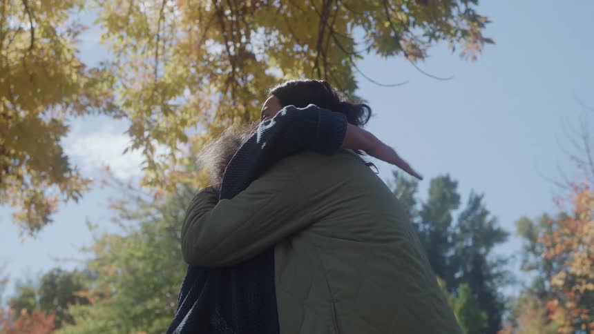 Two women hug while standing in a park on a sunny autumn day