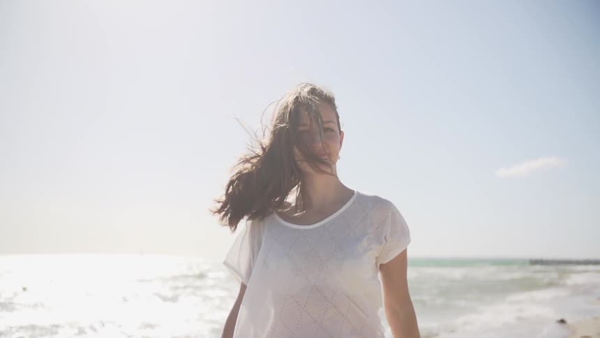 Woman walks across the shore and looks back