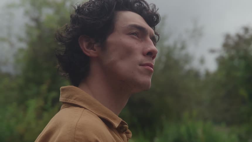 A mans head and shoulder are seen in profile against a background of green trees and gray sky while the man moves his eyes up and maintains a neutral mouth position