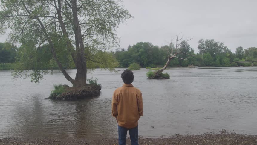 Man watches the calm river surrounded by trees under a cloudy sky
