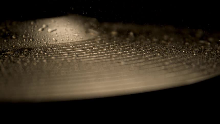 A golden plate being hit and releasing many particles of water droplets upwards