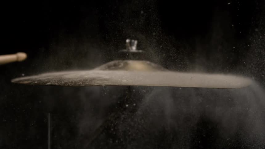 A drumstick hitting a cymbal and releasing a lot of dust into the air