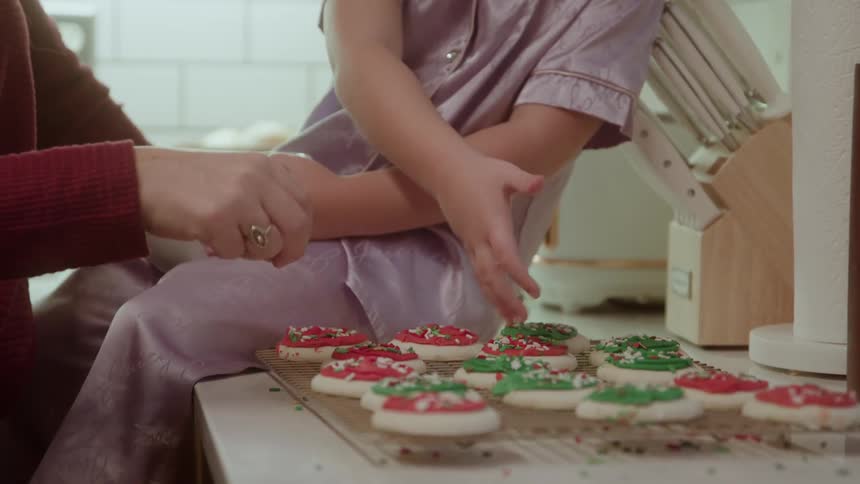 Child decorating colorful christmas cookies with the help of an adult