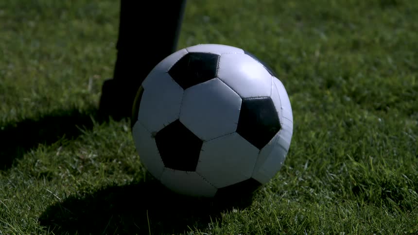 A persons foot kicking a black and white soccer ball on a lawn