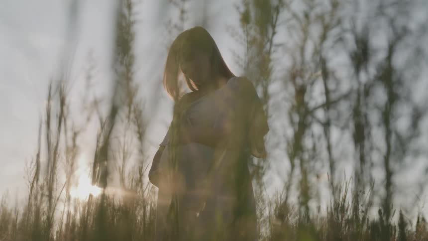 Expectant mother hugs her abdomen while standing in an overgrown field