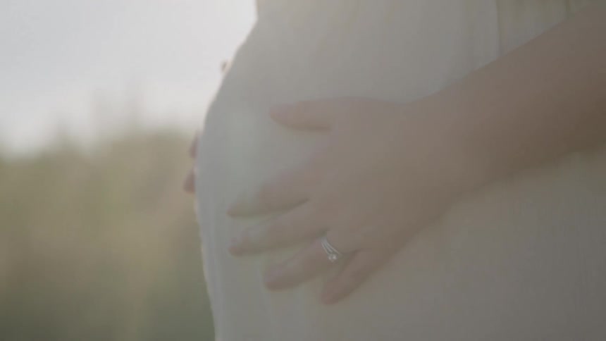 Hands resting on a pregnant womans belly outdoors