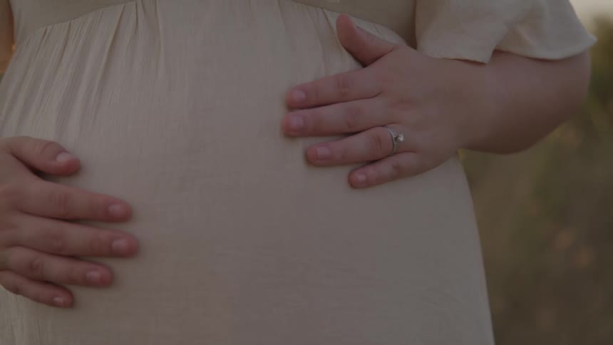 Expectant mother standing outdoors during the daytime caresses her abdomen