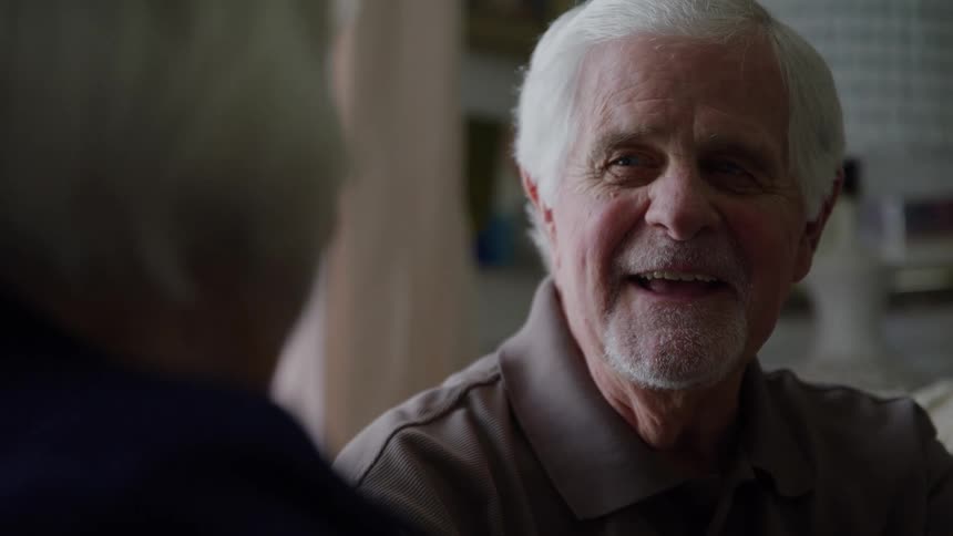 An elderly man with white hair and a kind face smiles warmly while in conversation