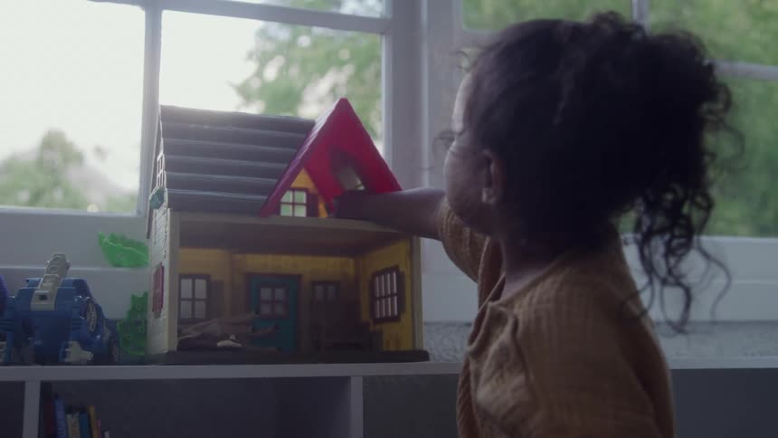 Girl plays with a dollhouse near the window on an autumn day