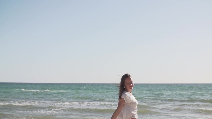 A woman raises her arms on a beach