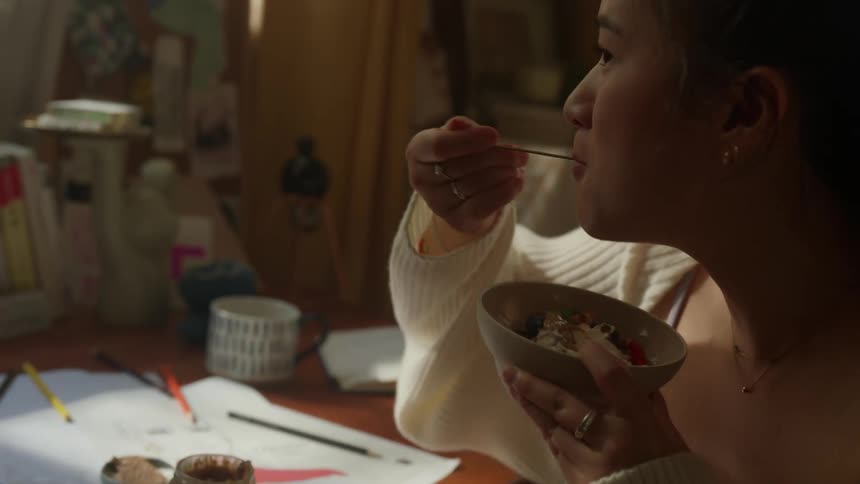 Woman dances in a chair in her bedroom while eating