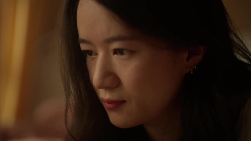 A young woman places two hands on a portable computer keyboard to scroll then looks down at the screen with an initially neutral facial expression that briefly becomes a slight smile in an indoor setting