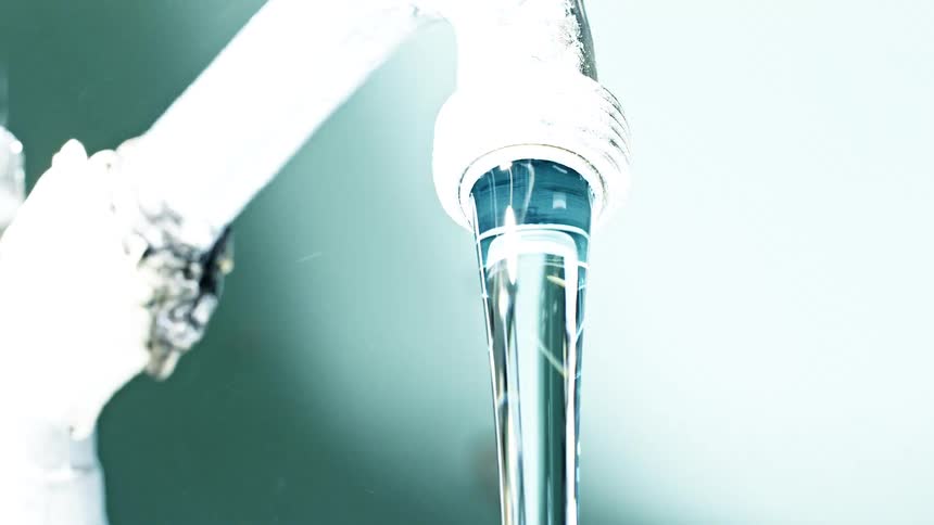 A close view of a shiny metal faucet shows a steady stream of clear running water against a bright softly blurred background