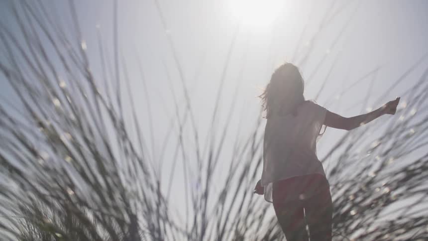 A person dances in the sunlight beside tall grass