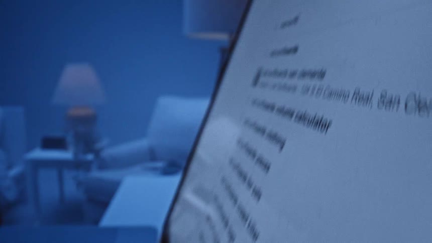 A closeup view shows a persons fingers pressing keys on a keyboard while a computer monitor displays text in a dark room
