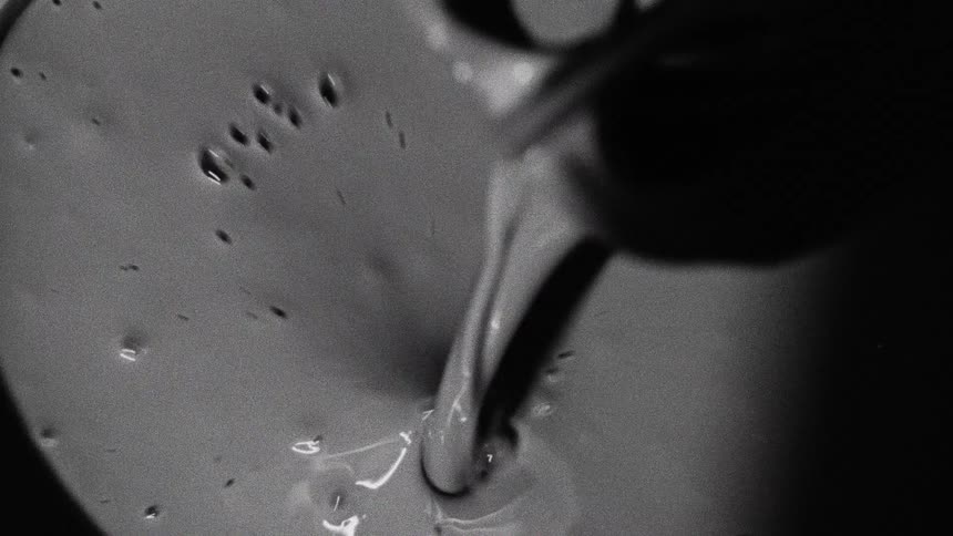 Thick liquid being poured forming bubbles on the surface in black and white