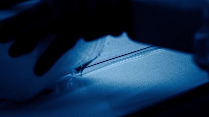 Hand pours liquid over a surface lit in deep blue tones