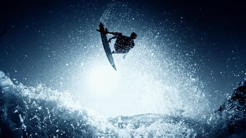 Surfer performing an aerial jump above the waves surrounded by illuminated splashes