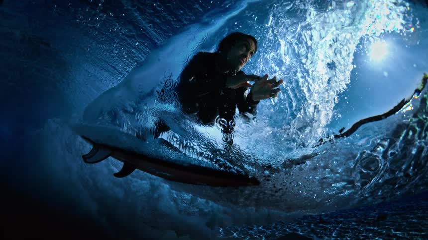 Surfer gliding inside the barrel of a wave lit by blue light