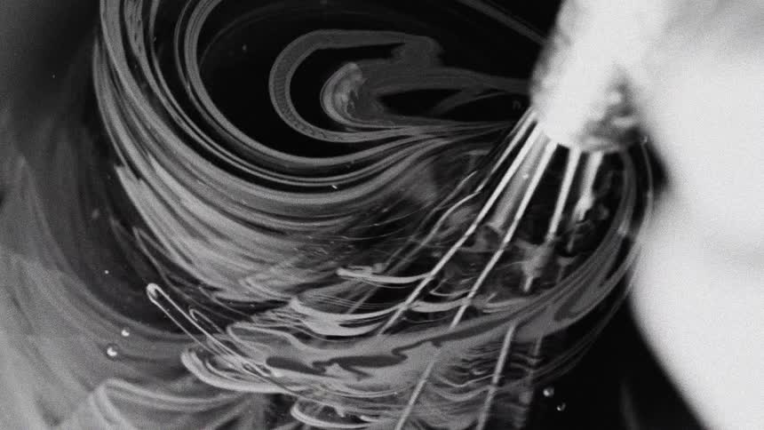 Whisk stirs dark liquid creating swirls in black and white