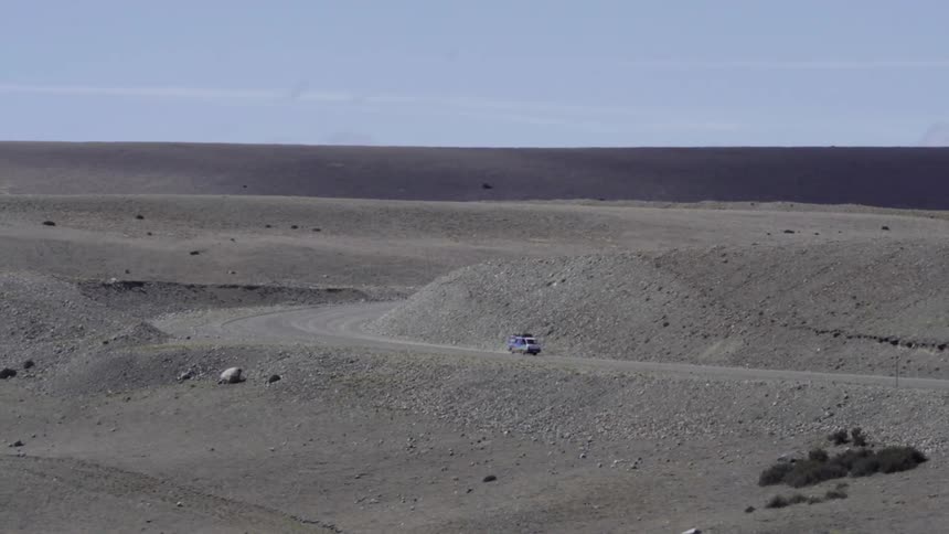 A vehicle drives in the desert on a sunny day