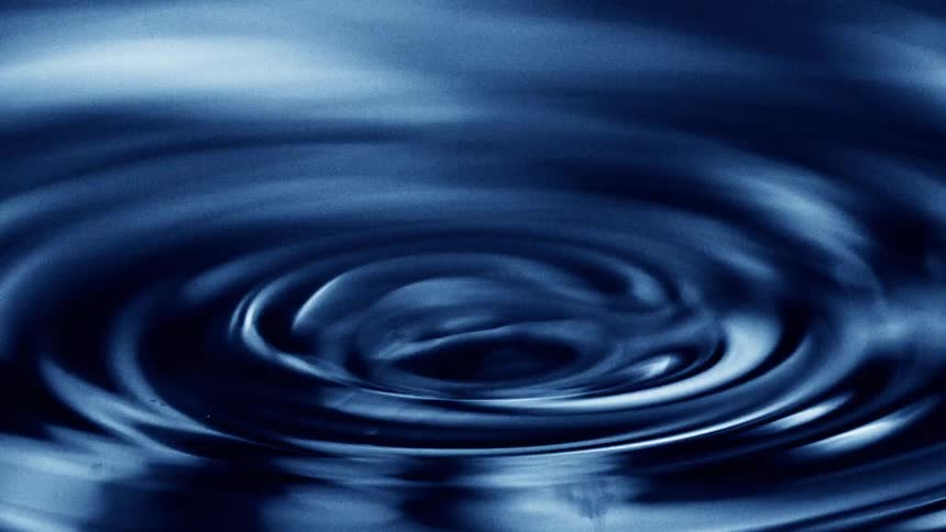 Blue water droplet forming concentric circles on the liquid surface