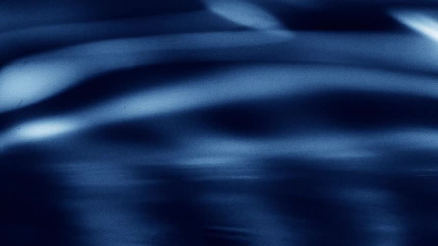 Blue water surface forming gentle ripples around a droplet about to fall