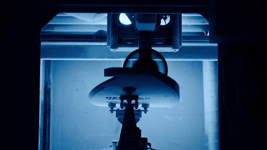 Surfboard being shaped in an automated machine under blue light