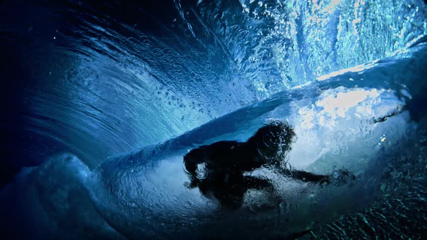 Surfer riding inside a wave illuminated in shades of blue
