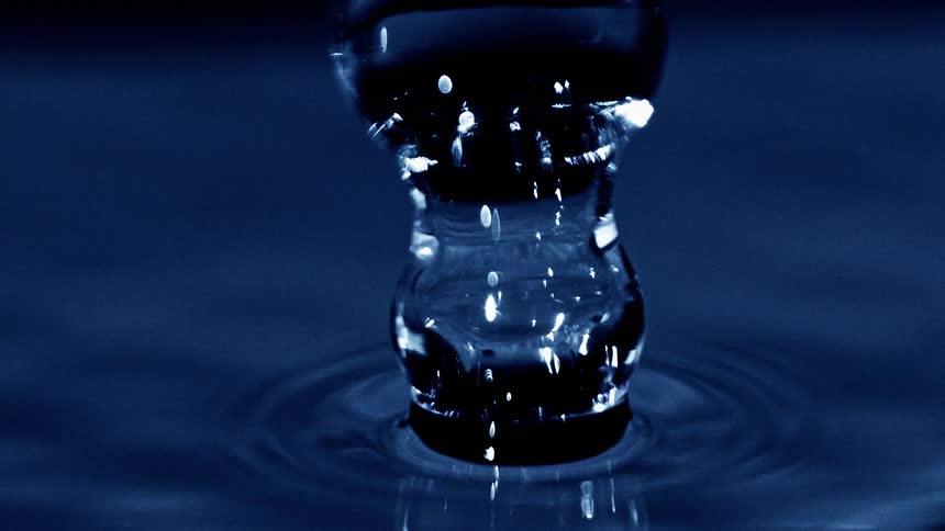 Water column rises from droplet impact on blue liquid surface forming concentric ripples