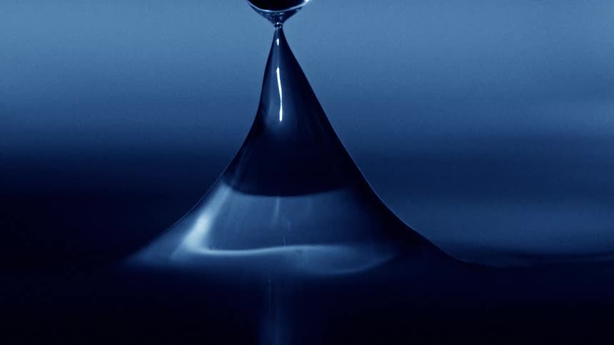 A water droplet hits the surface of a glass of water creating a ripple effect that gently spreads outward