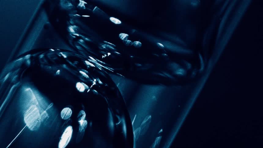A closeup of clear liquid with clustered bubbles under deep blue lighting creating glossy curved reflections