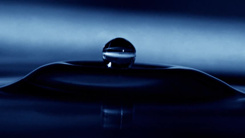 Blue water drop suspended falling into water and forming a splash