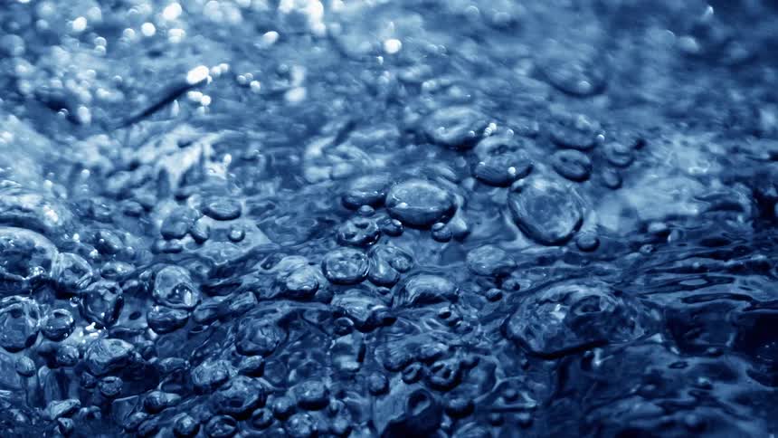 A churning close up of dark blue water shows bubbles and ripples colliding across the surface