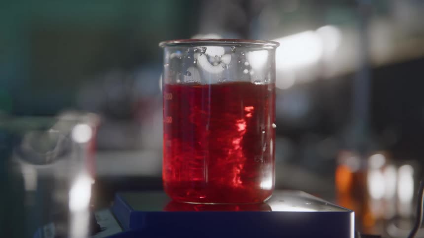 The video is a closeup of a beaker containing a vibrantly red liquid in a laboratorythe liquid is actively being stirred by a submerged magnetic stirrer bar creating a visible vortex