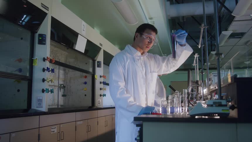 Young male scientist examining a test tube filled with a purple liquid on a lab next to another female scientist indoors