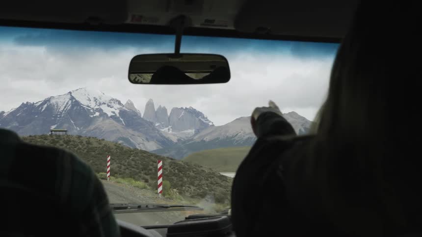 While riding in a car, a woman points at the snow covered peaks ahead