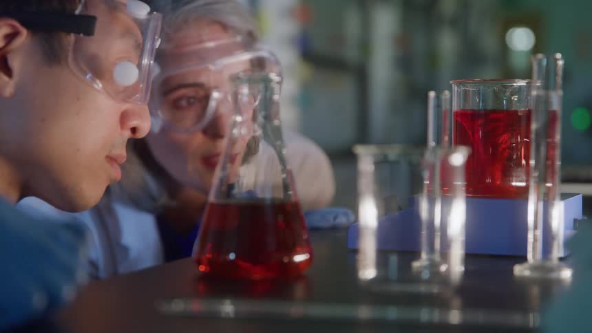 Man and woman analyzing red liquid in glass flasks during laboratory activity with protective equipment