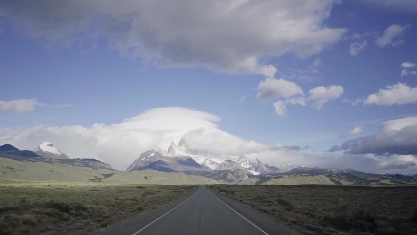 A view of snow capped mountains off in the distance with clouds above them