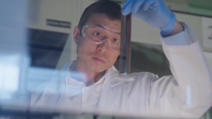 Scientist holding and observing a graduated cylinder with colored liquid in a laboratory