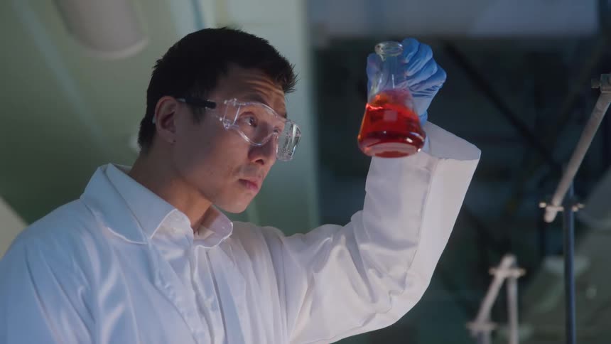 Young male scientist examining a glass flask filled with a red liquid indoors