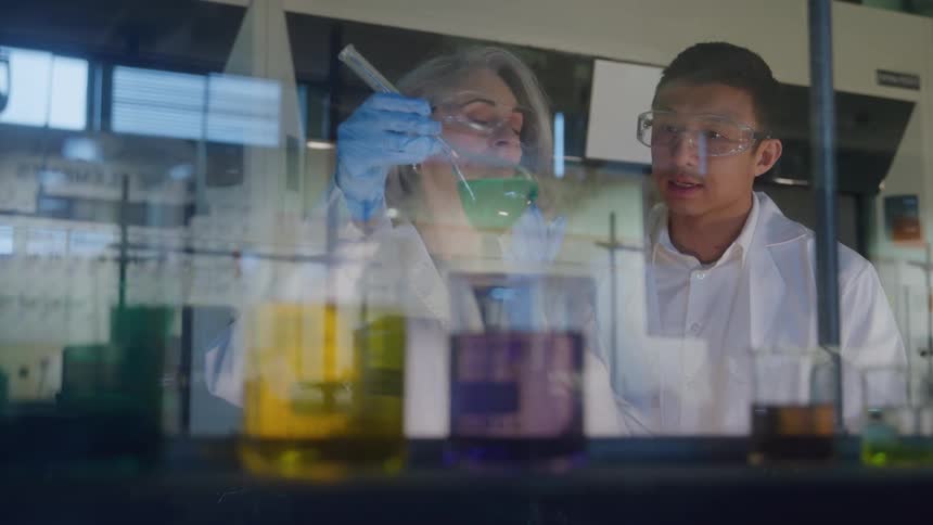 Two scientists analyzing colorful samples in glass containers in the laboratory