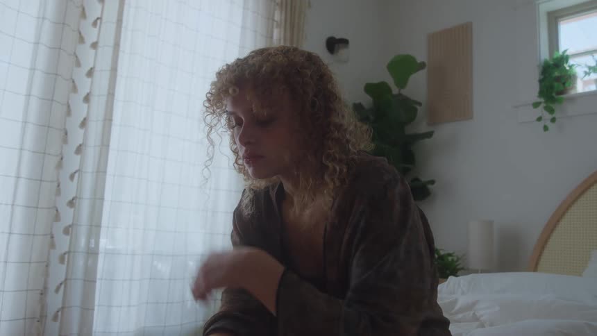 A sad depressed woman sits alone on a bed at home