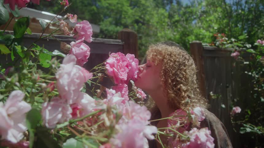A young woman admiring and perceiving a pink rose flower in an outdoor garden during daytime