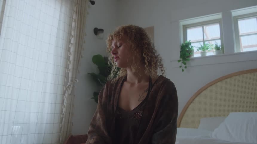 The woman is sitting on the bed at home