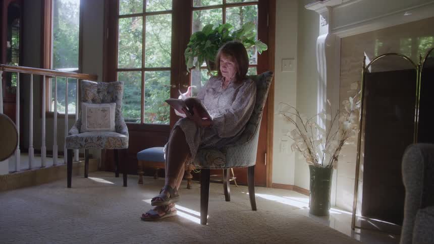 A middle aged woman reading a book while sitting indoors during daytime