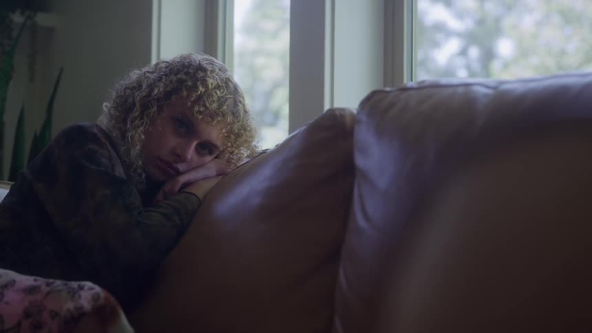 Woman lying on the couch with a pensive expression gazing toward the bright window