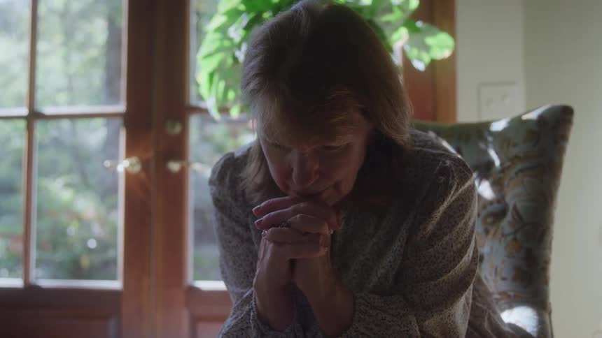 The woman is praying as she sits on the chair
